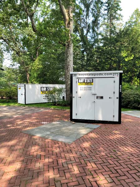 Two Bay State storage pods on brick pavers by a tree.